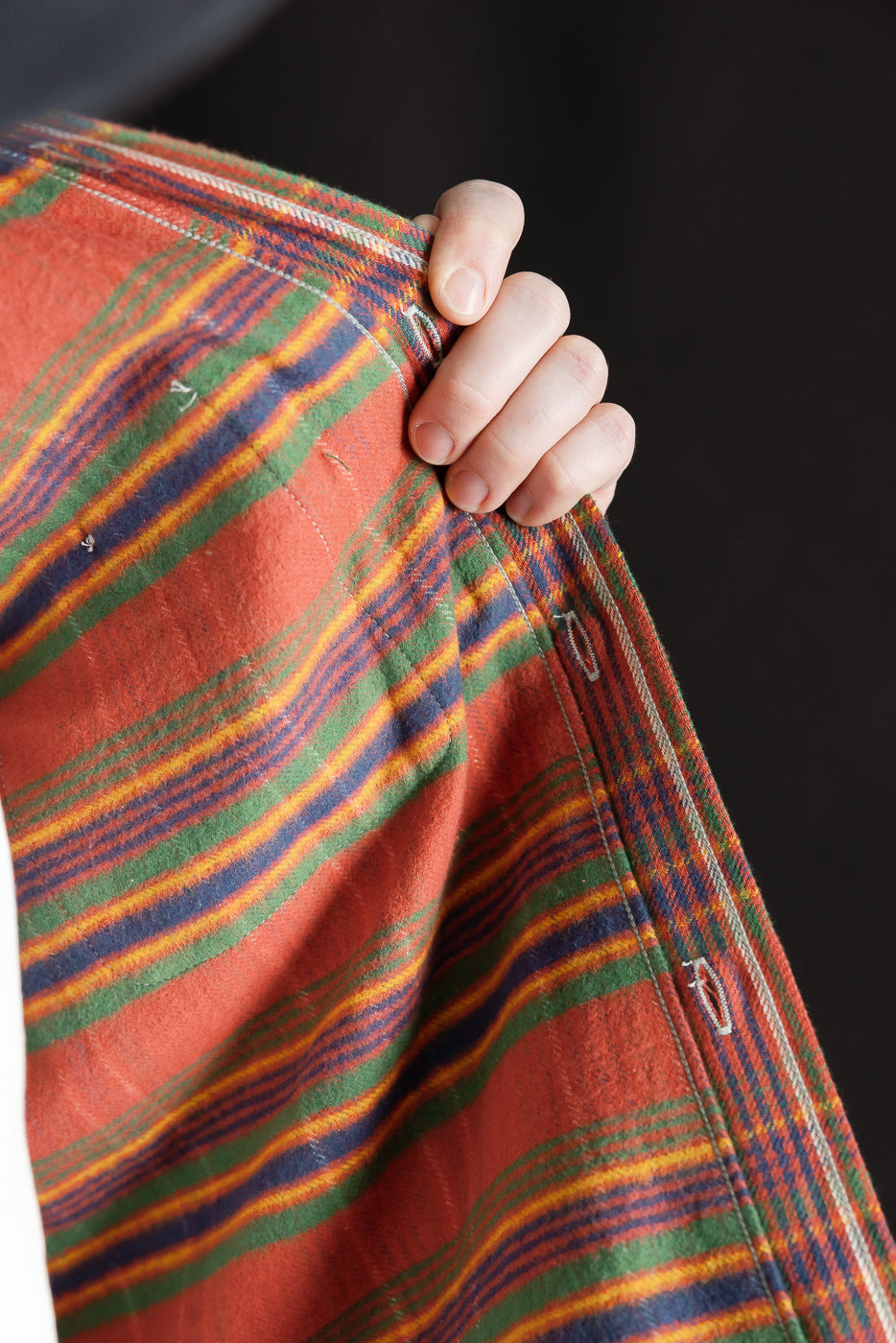 Close-up of buttonhole side front panel on red striped flannel shirt, showing fabric texture and stitching detail.