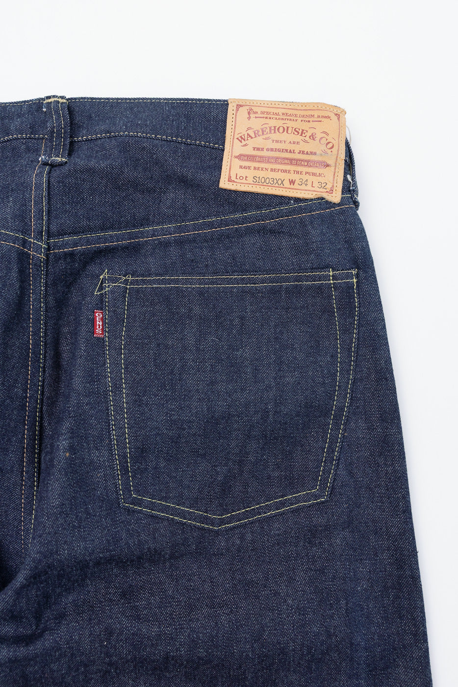 Close-up of the back waist and right pocket of dark blue selvedge jeans with a leather tag.