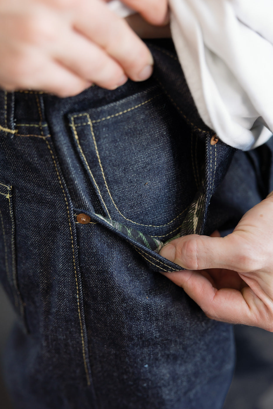 Close-up of the back right pocket of dark indigo selvedge denim jeans being held open.