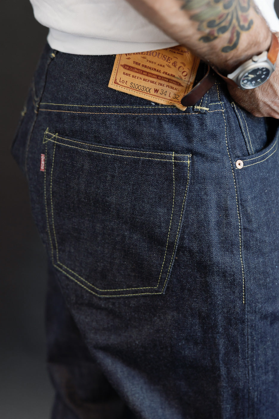 Close-up side view of dark indigo selvedge denim jeans showing rear pocket and leather patch.