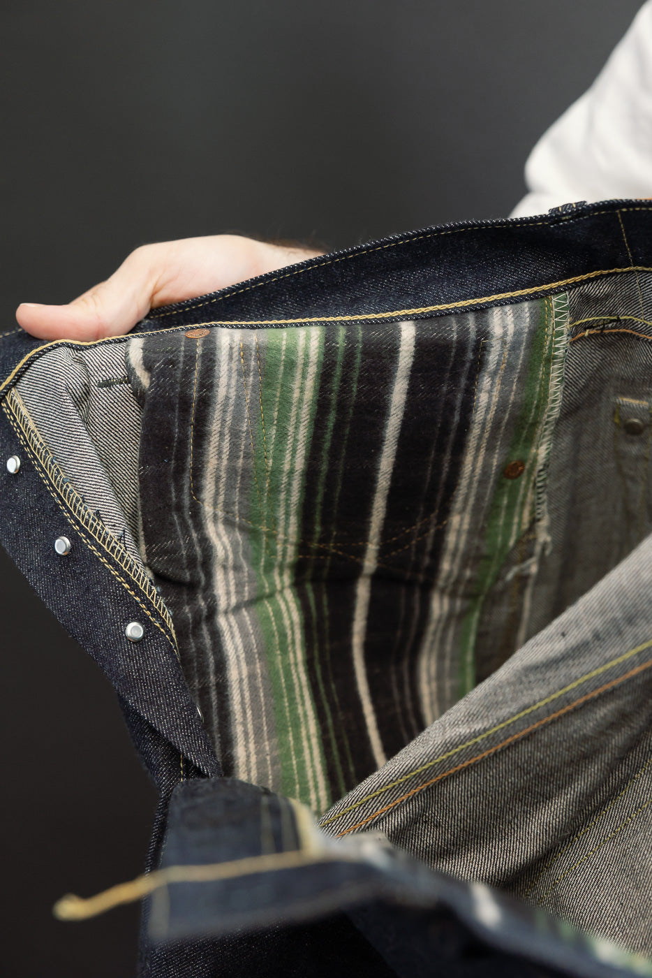 Close-up view of the interior waist and pocket lining of dark selvedge denim jeans showing green stripe pattern.