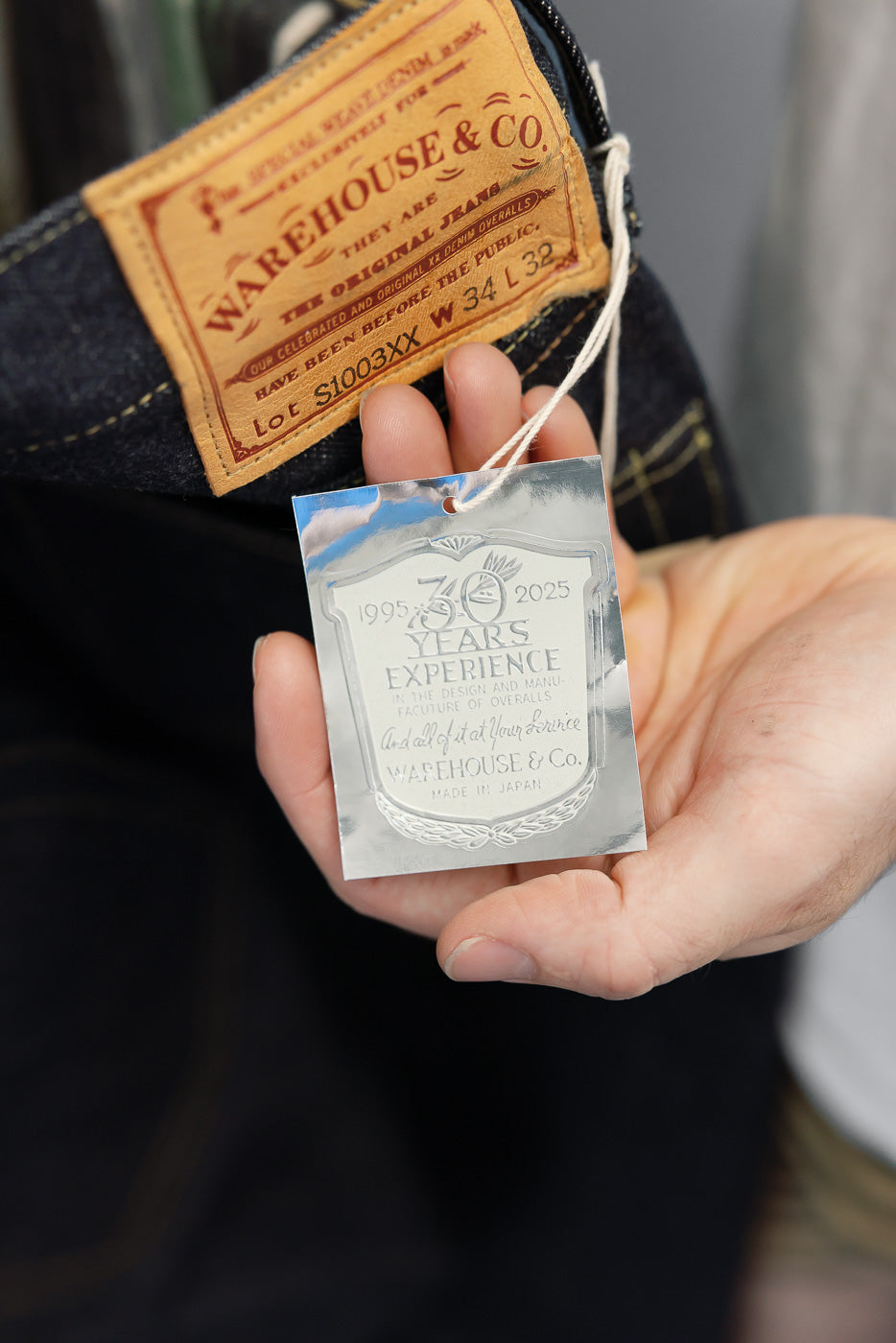 Close-up of a male hand holding a 30th anniversary metal tag and leather waist label of denim jeans.