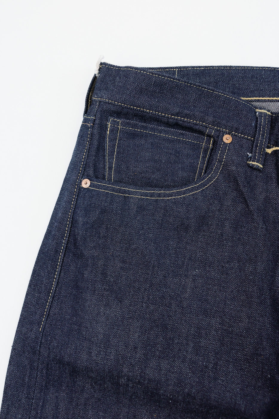 Close-up of the front right hip of dark indigo selvedge denim jeans showing pocket and rivets.