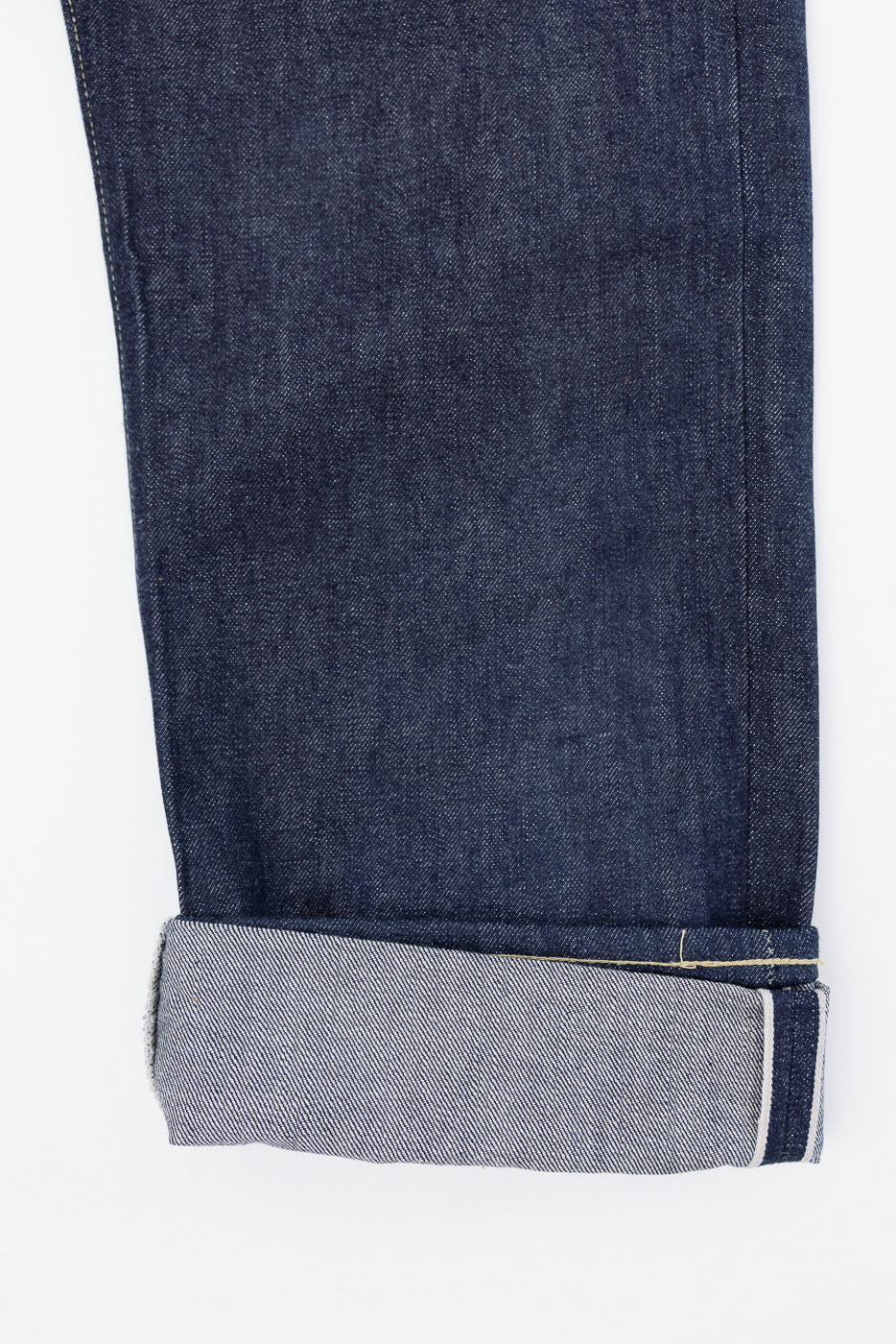 Close-up of the bottom hem and selvedge cuff on the front of dark indigo denim jeans.