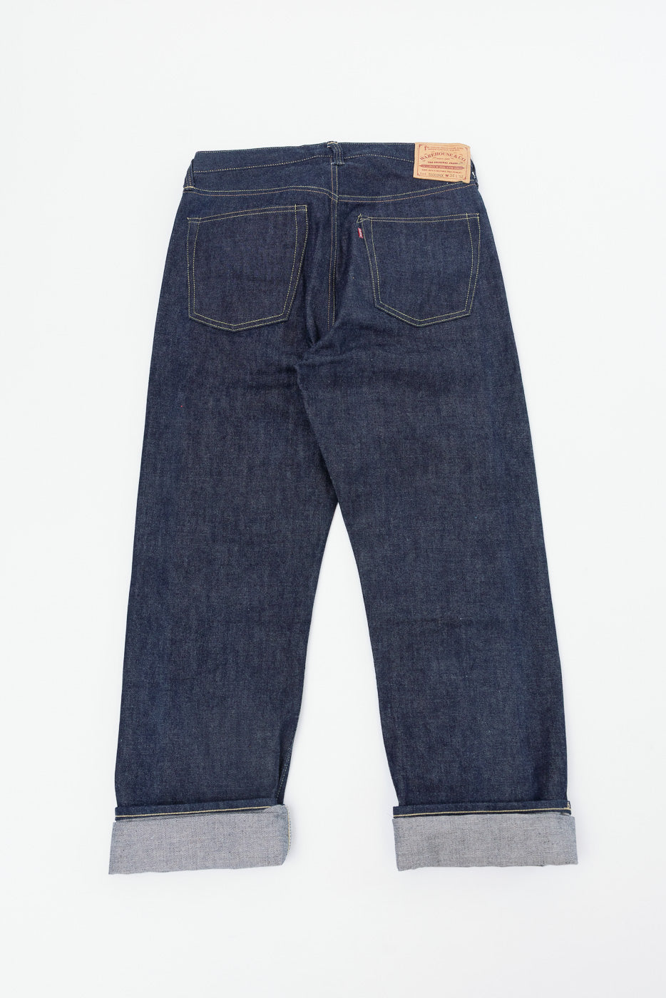 Flat lay showing the back of dark indigo selvedge denim jeans with cuffed hems.