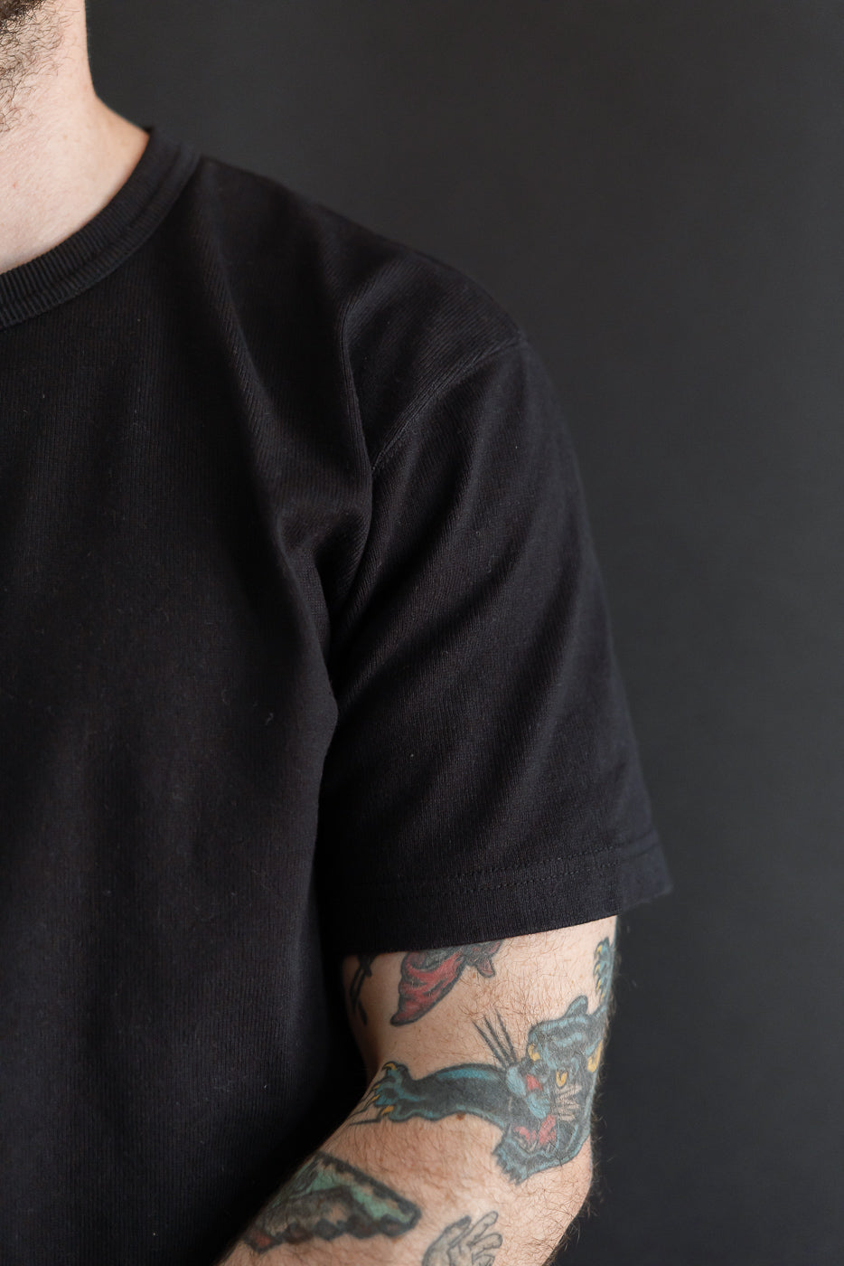 Close-up of the sleeve and collar of a black t-shirt on a male model, 5'9