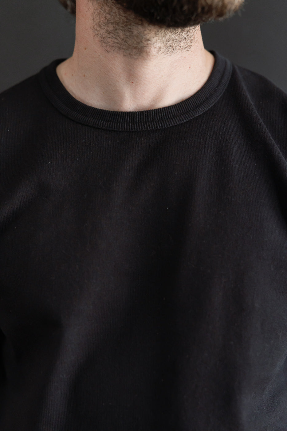 Close-up of the front neckline of a black sweatshirt on a male model, 5'9