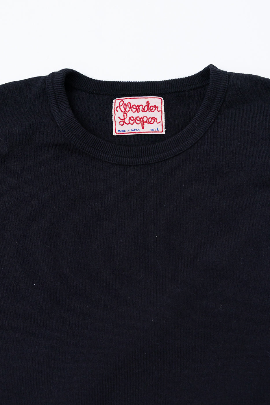 Close-up of the back neckline and red Wonder Looper brand tag on a black crewneck sweatshirt.