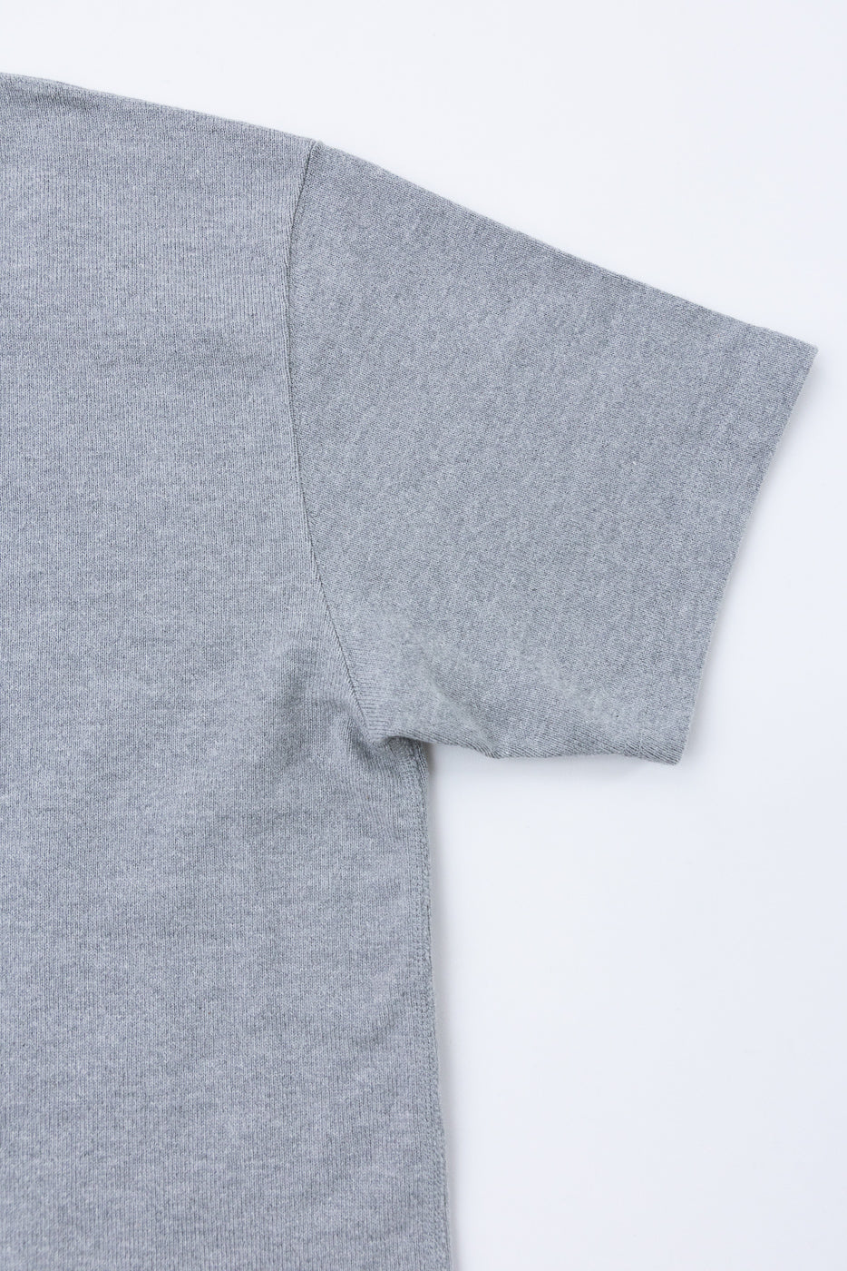 Close-up flat lay of the right sleeve and side of a grey heathered fabric t-shirt.