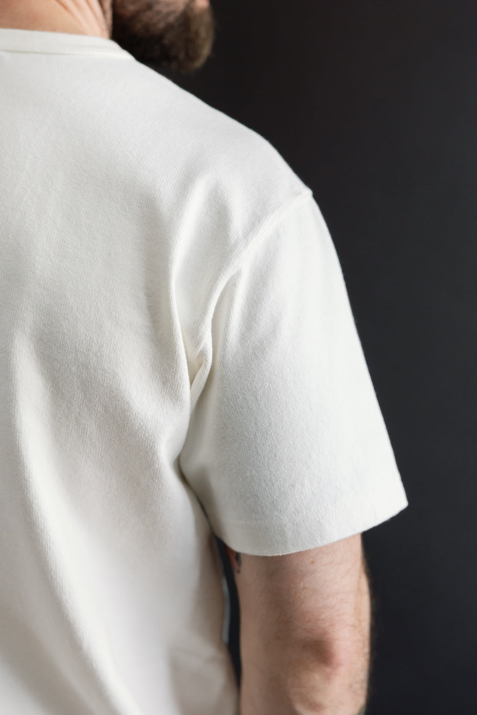 Close-up of the back and right sleeve of a white t-shirt on a male model, 5'9