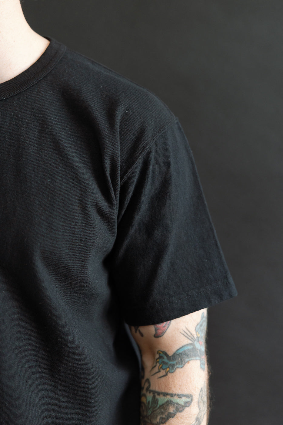 ELS Recycled Cotton Slub Crewneck T-Shirt - Black, showcasing a close-up of the right arm adorned with traditional tattoos, highlighting the T-shirt's soft, textured fabric and modern athletic fit.