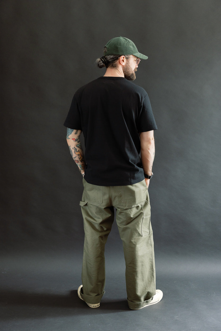 A man with a beard and glasses models the ELS Recycled Cotton Slub Crewneck T-Shirt - Black, showcasing its modern athletic fit paired with olive-green cargo pants and off-white sneakers.