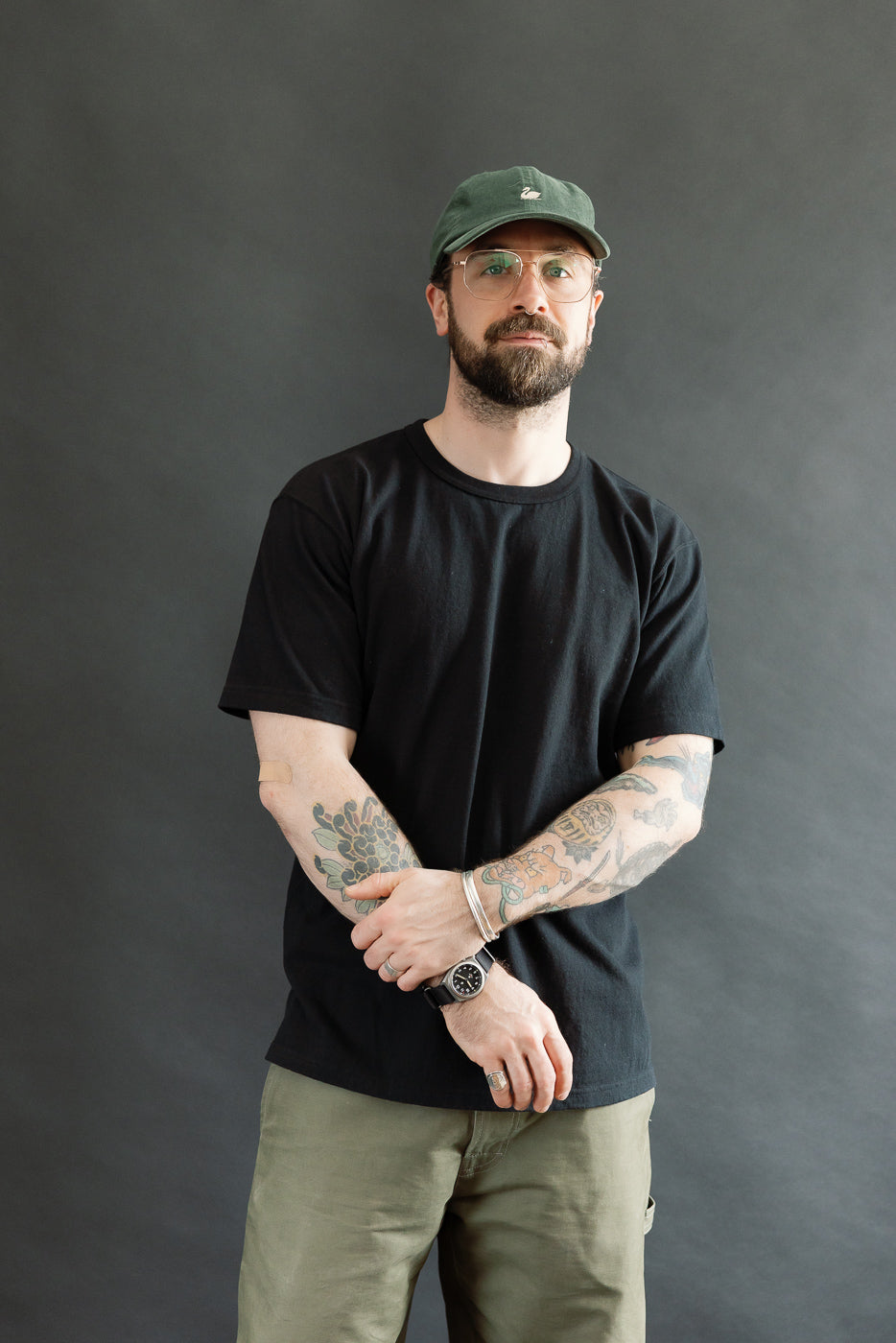 A man models the ELS Recycled Cotton Slub Crewneck T-Shirt - Black, showcasing its modern athletic fit and textured Japanese fabric, complemented by tattoos and casual accessories.