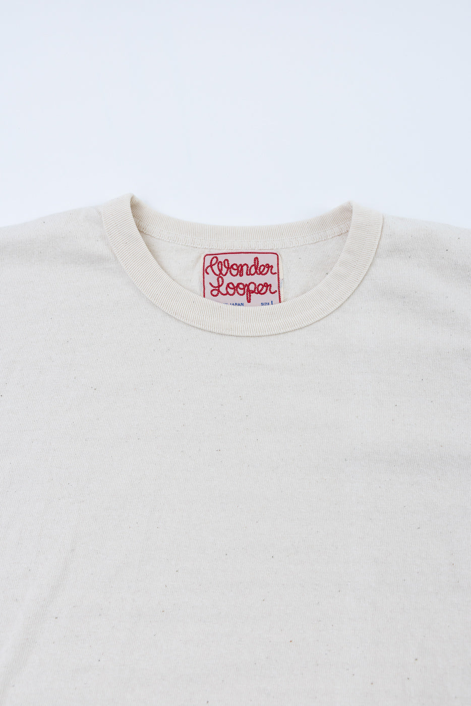 ELS Recycled Cotton Slub Crewneck T-Shirt - Ecru: Cream-colored, speckled T-shirt with ribbed crewneck, featuring a red-embroidered “Wonder Looper” label beneath the neckline, showcasing intricate Japanese craftsmanship.