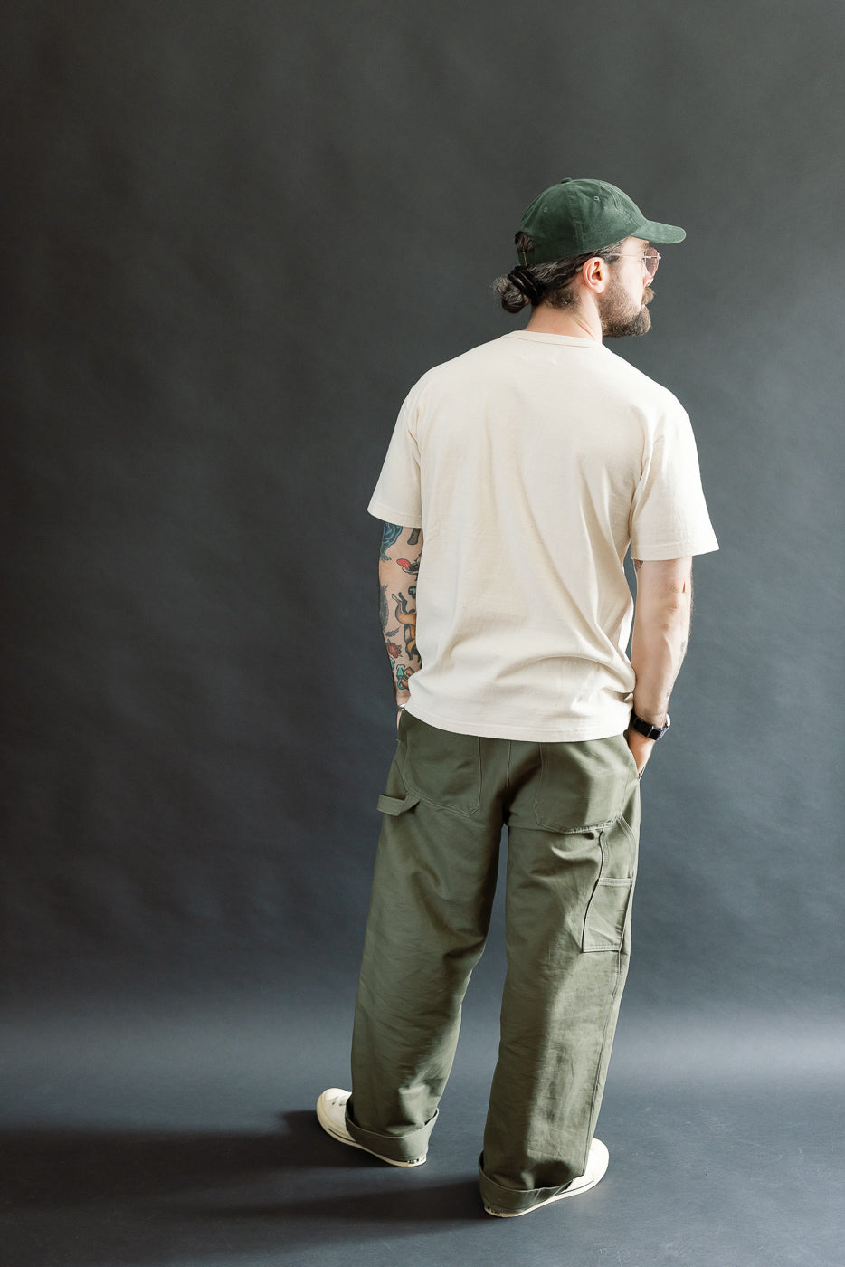 A male model showcases the ELS Recycled Cotton Slub Crewneck T-Shirt - Ecru, styled with olive cargo pants and a dark green cap, highlighting its athletic fit and textured fabric.