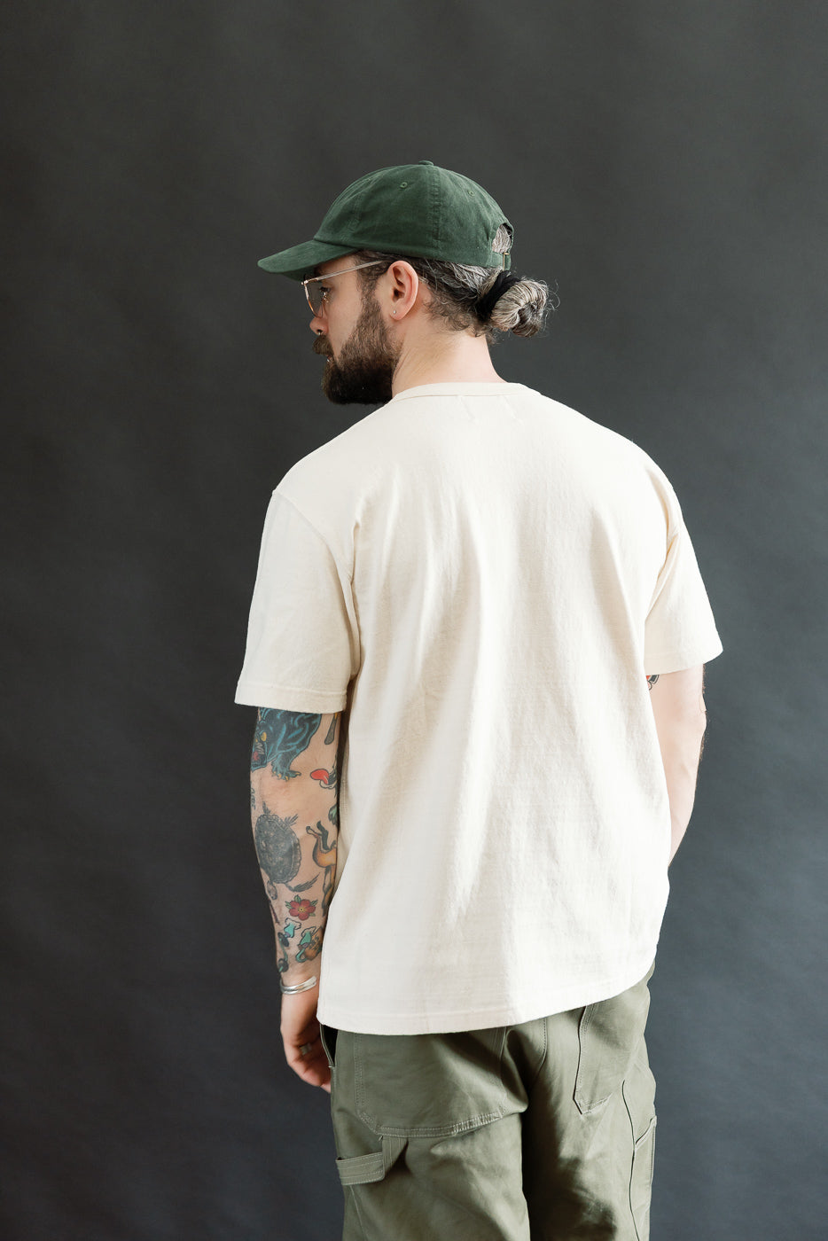 Man wearing the ELS Recycled Cotton Slub Crewneck T-Shirt - Ecru, seen from behind. The T-shirt features a modern athletic fit and is paired with olive-green cargo trousers, showcasing a casual style.