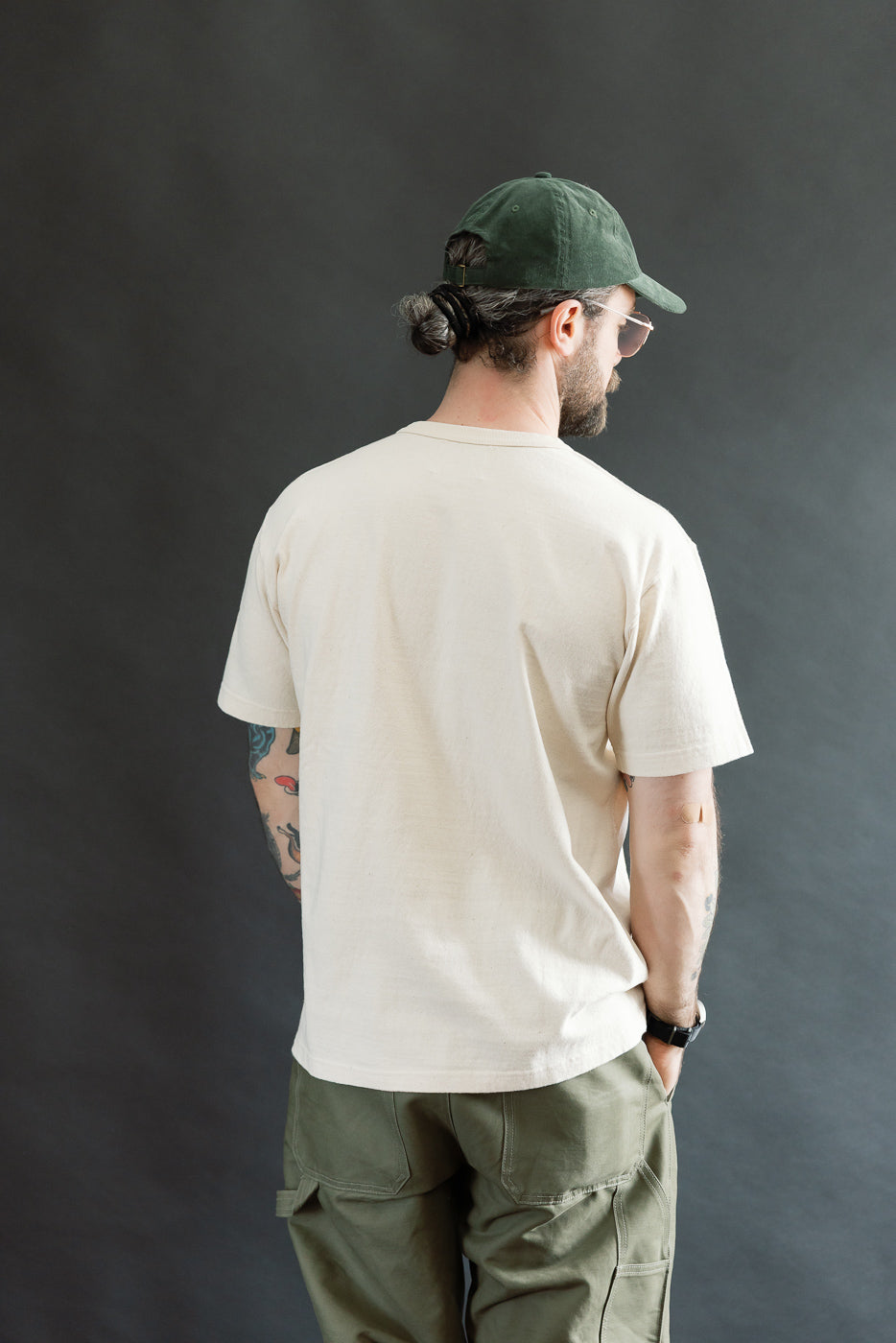 Man in ELS Recycled Cotton Slub Crewneck T-Shirt - Ecru, showcasing its athletic fit, ribbed collar, and textured fabric, paired with olive cargo pants and aviator sunglasses, embodying Dant's premium menswear style.