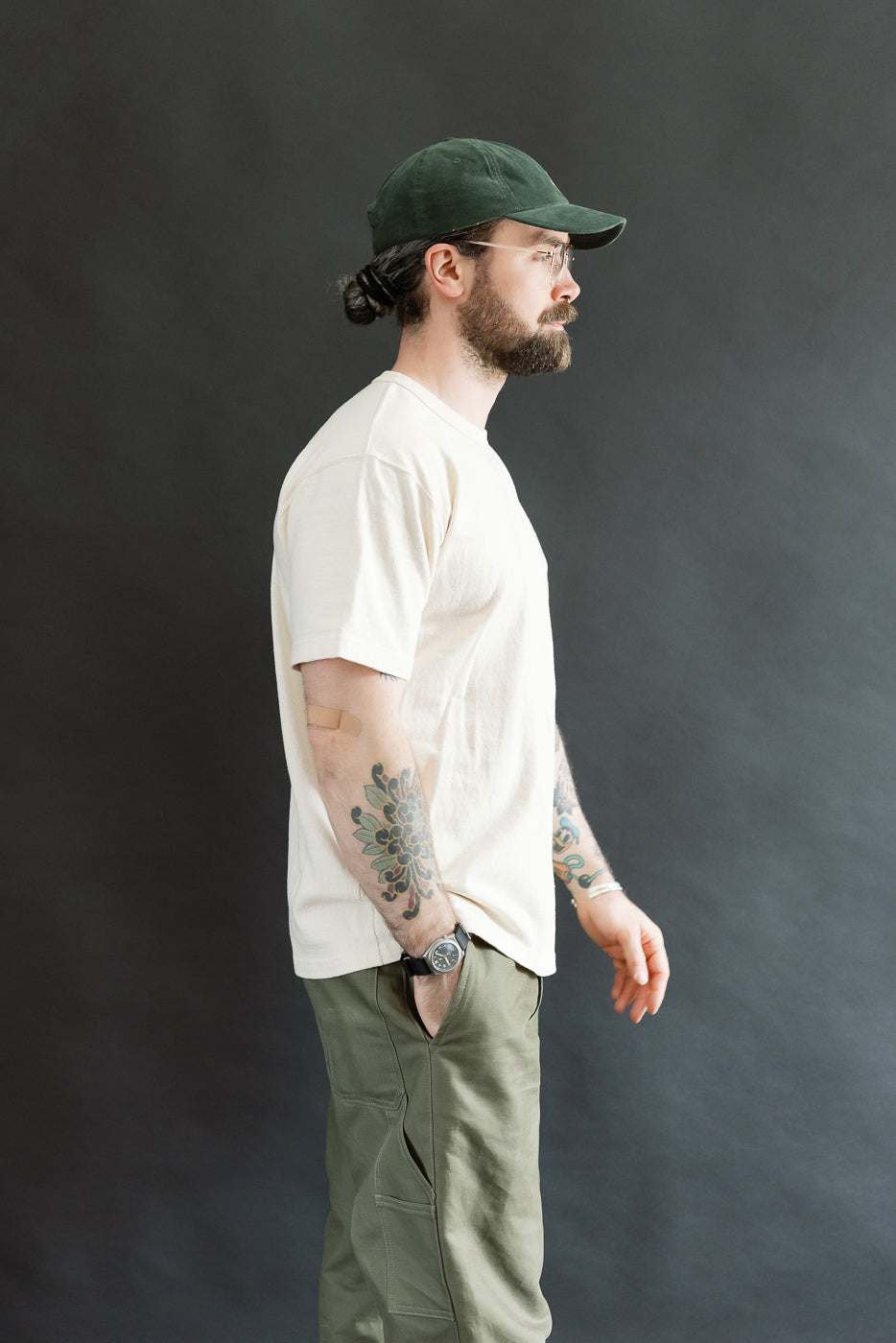 Man in profile wearing the ELS Recycled Cotton Slub Crewneck T-Shirt - Ecru, showcasing its modern athletic fit. He pairs it with olive cargo pants, highlighting a casual, stylish look.