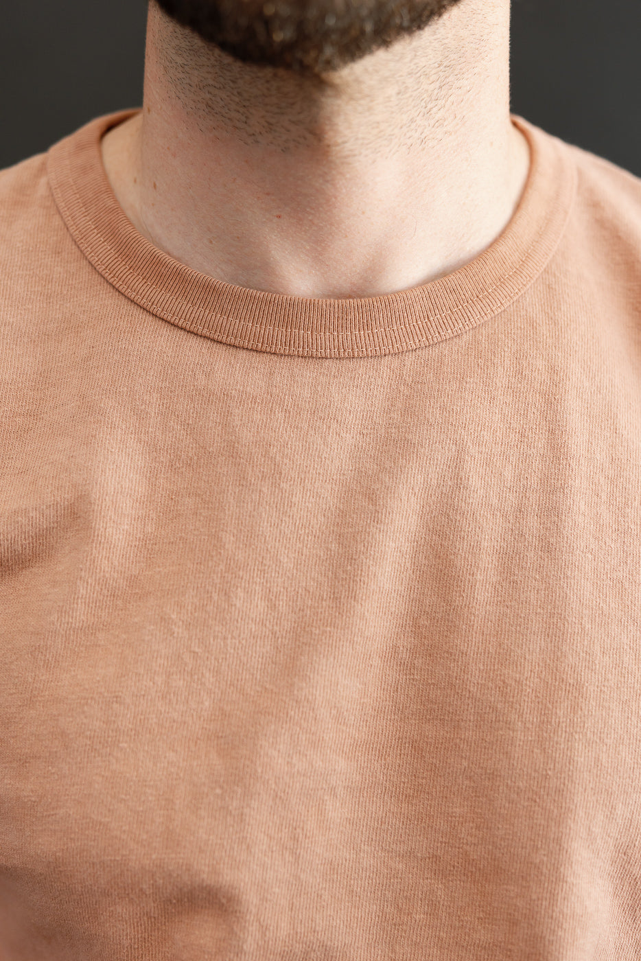 Close-up front view of male model wearing peach crewneck tee, showcasing ribbed collar and fabric texture