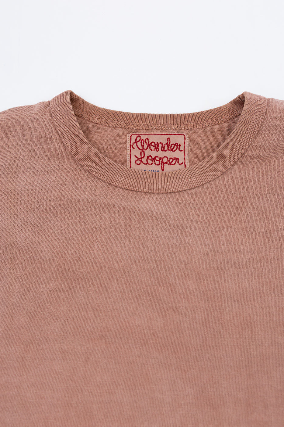 Close-up of dusty rose t-shirt collar with 'Wonder Looper' tag, front view, soft fabric texture