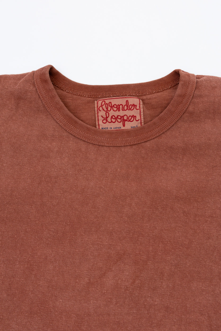 Close-up front view of rust-colored tee showing Wonder Looper neck tag, ribbed collar, and fabric texture