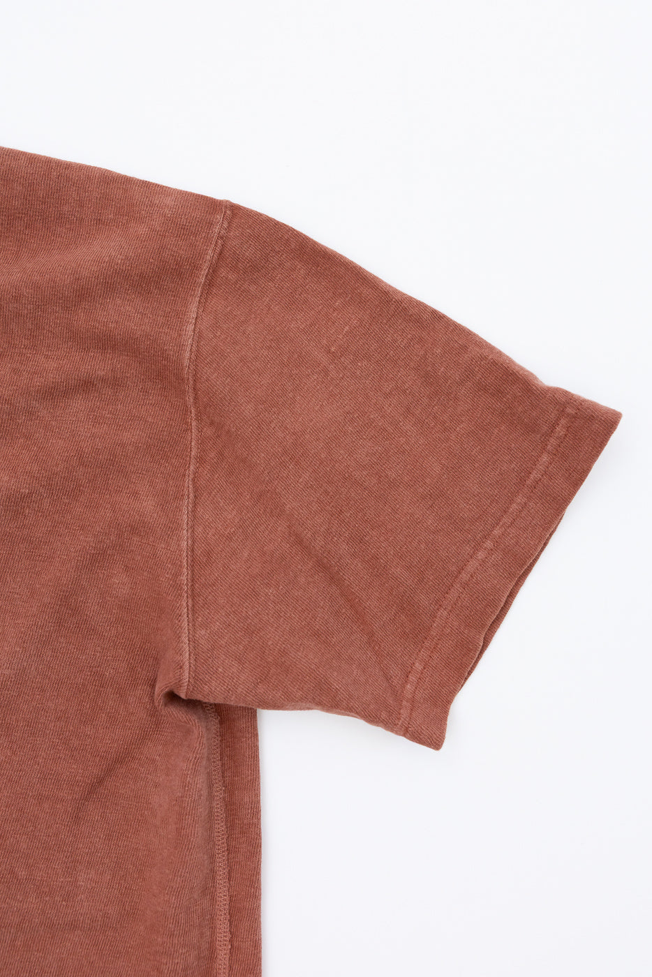 Close-up front view of rust-colored tee shirt sleeve, showing ribbed texture and clean hem detail