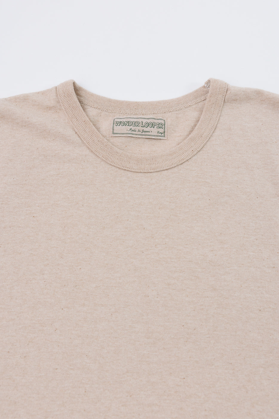 Close-up front view of beige crew neck tee showing Wonder Looper tag, ribbed collar, and soft cotton texture.