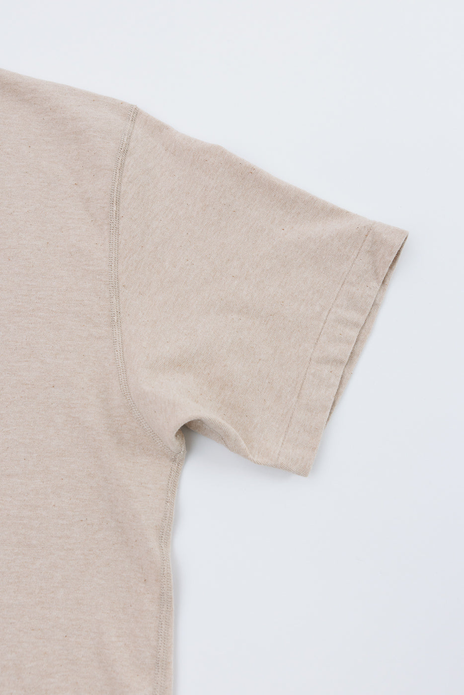 Close-up front view of beige t-shirt sleeve, showing ribbed hem and shoulder seam detail on flat lay