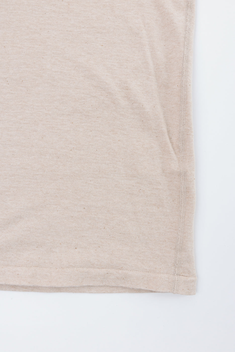 Close-up of beige t-shirt hem and side seam, showing fabric texture and stitching detail
