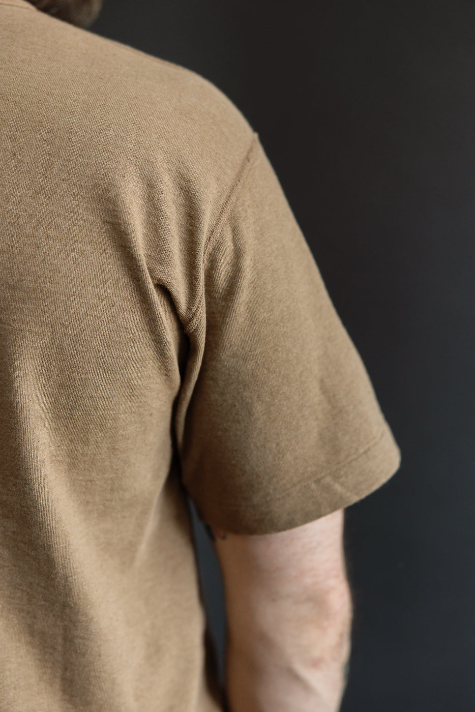 Close-up of male model's back shoulder, showcasing tan t-shirt sleeve and fabric texture