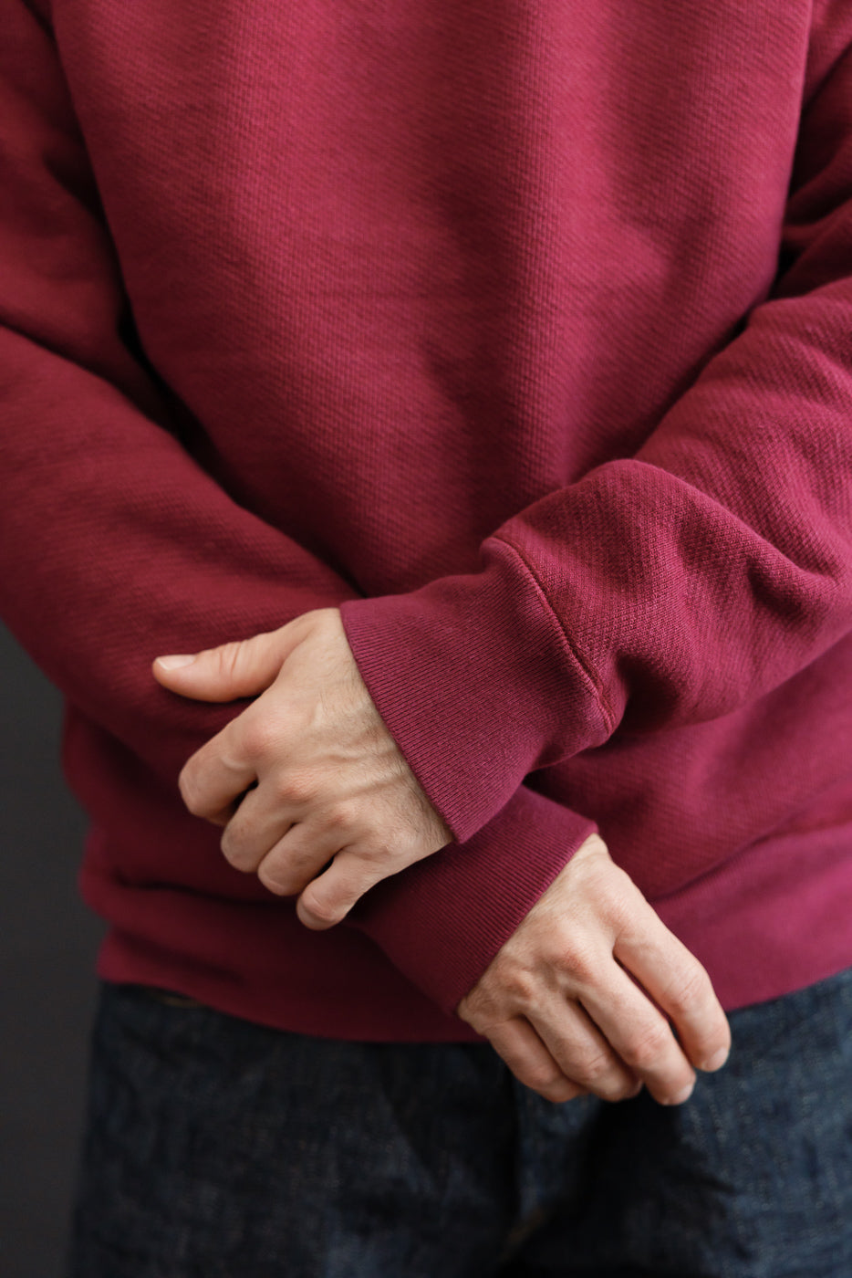 Close-up of the front of a male model's maroon textured sweatshirt sleeves and hands.