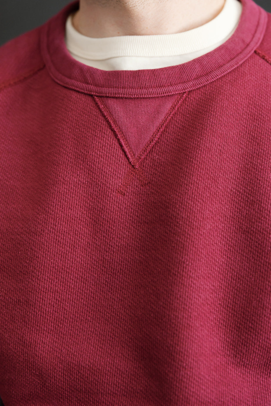 Close-up front view of a maroon crewneck sweatshirt showing ribbed collar and V-stitch detail.