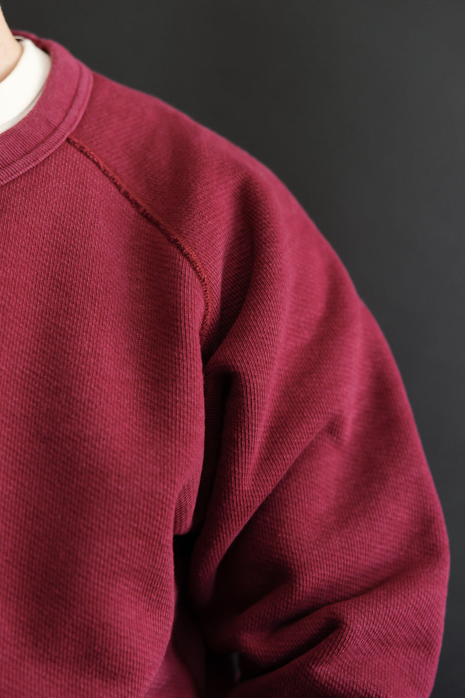 Close-up of the left shoulder and sleeve texture of a maroon crewneck sweatshirt.