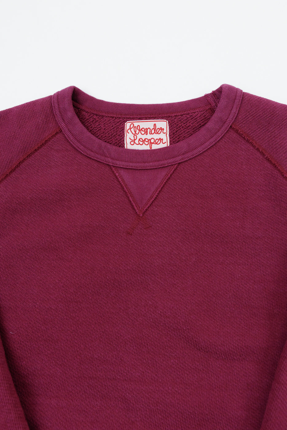 Close-up of the front neckline and Wonder Looper tag on a maroon crewneck sweatshirt.