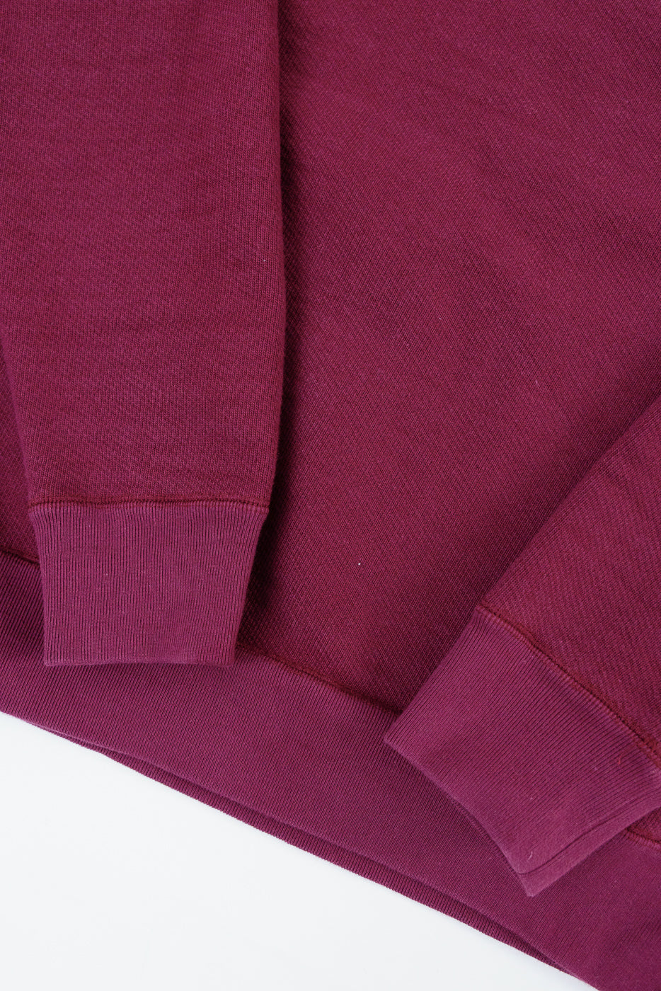 Close-up of the front lower hem and ribbed cuffs of a burgundy sweatshirt.