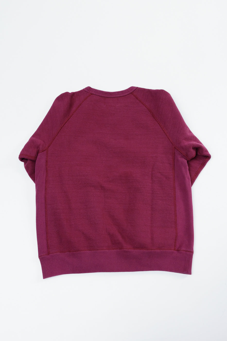 Flat lay showing the back of a maroon crewneck sweatshirt with ribbed cuffs and hem.