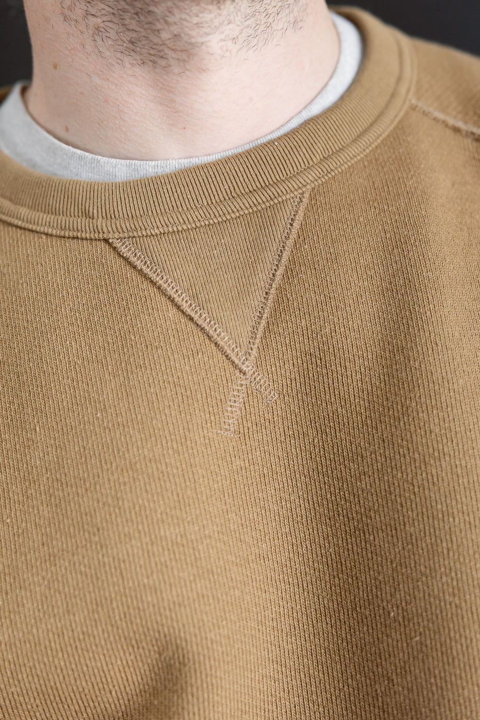 Close-up of front neckline and stitching on dune brown Wonder Looper pullover crewneck, shown on male model, 5'9