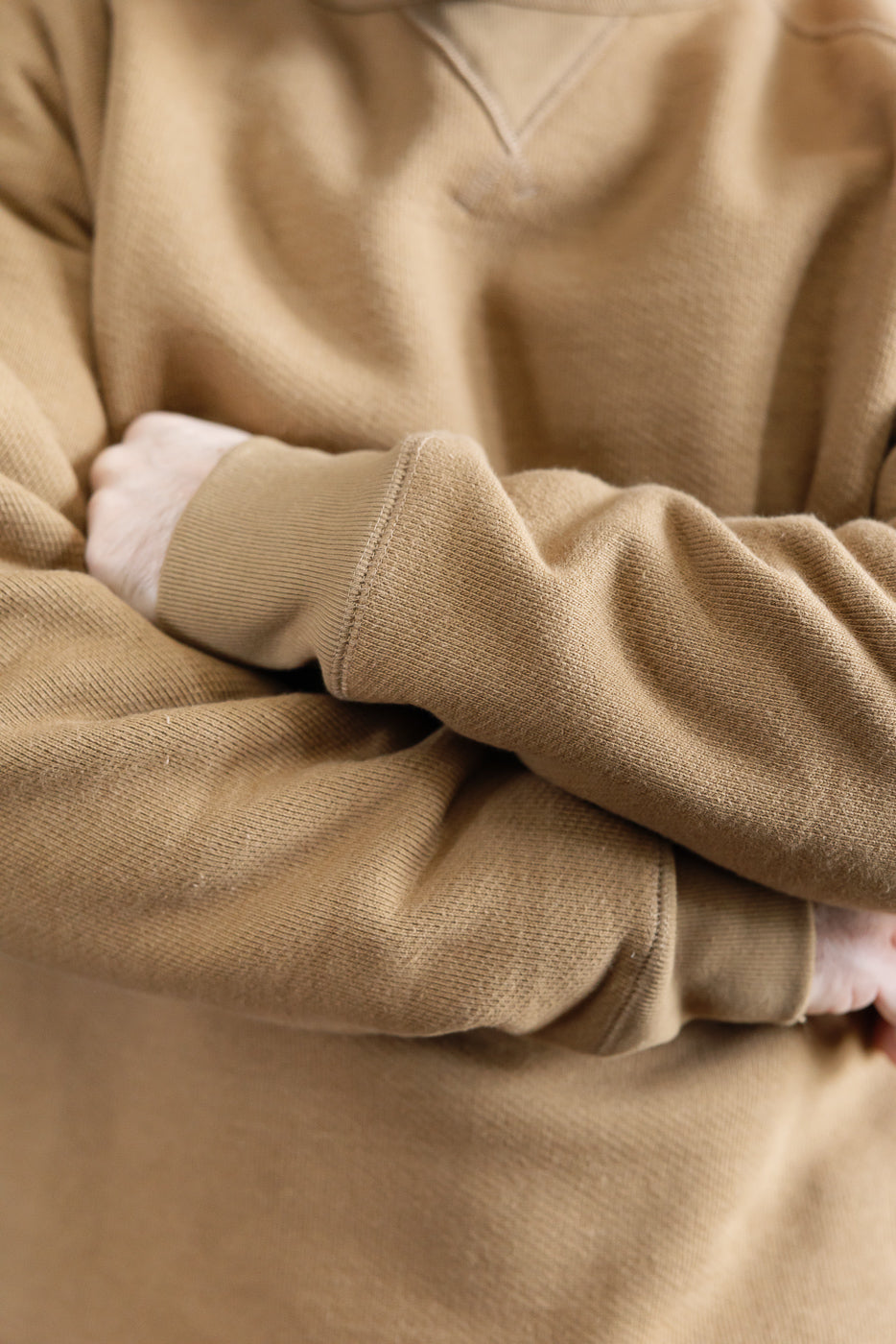 Close-up of male model's arms in tan Wonder Looper pullover crewneck, front, fabric texture detail.