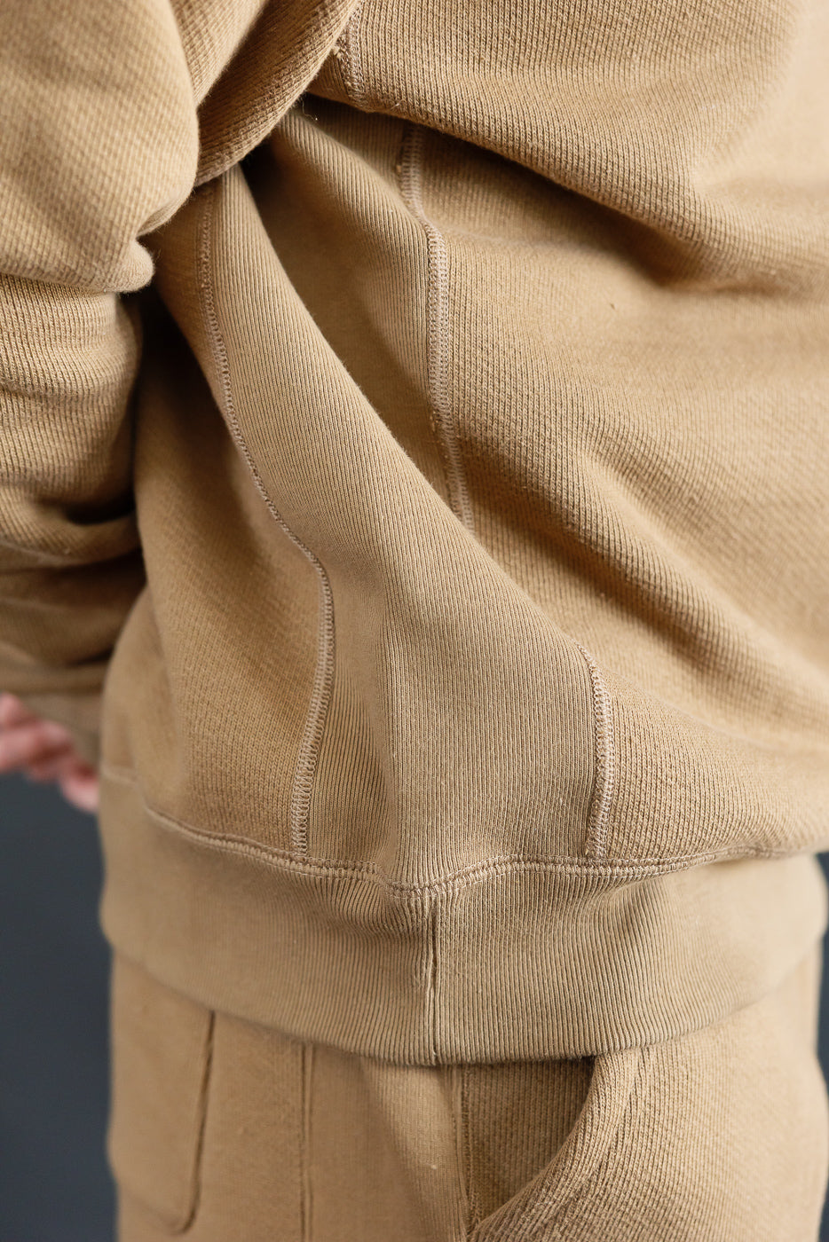Close-up of side seam and hem on Wonder Looper dune double heavyweight French terry pullover crewneck, showing fabric texture and stitching details on male model, Dant shop.