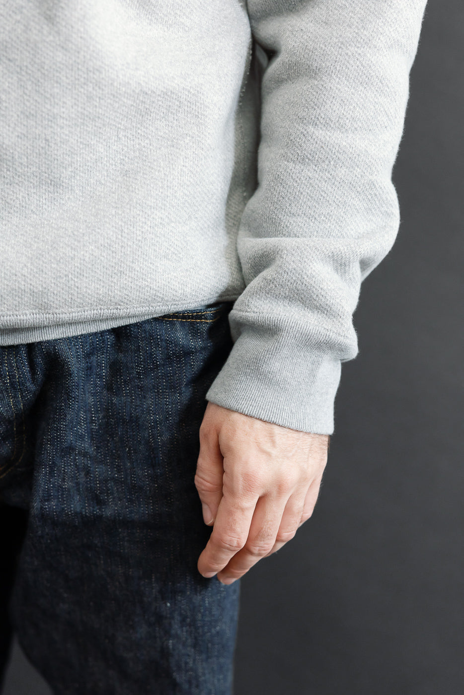Close-up of the front of a male model's grey sweater and dark denim jeans.
