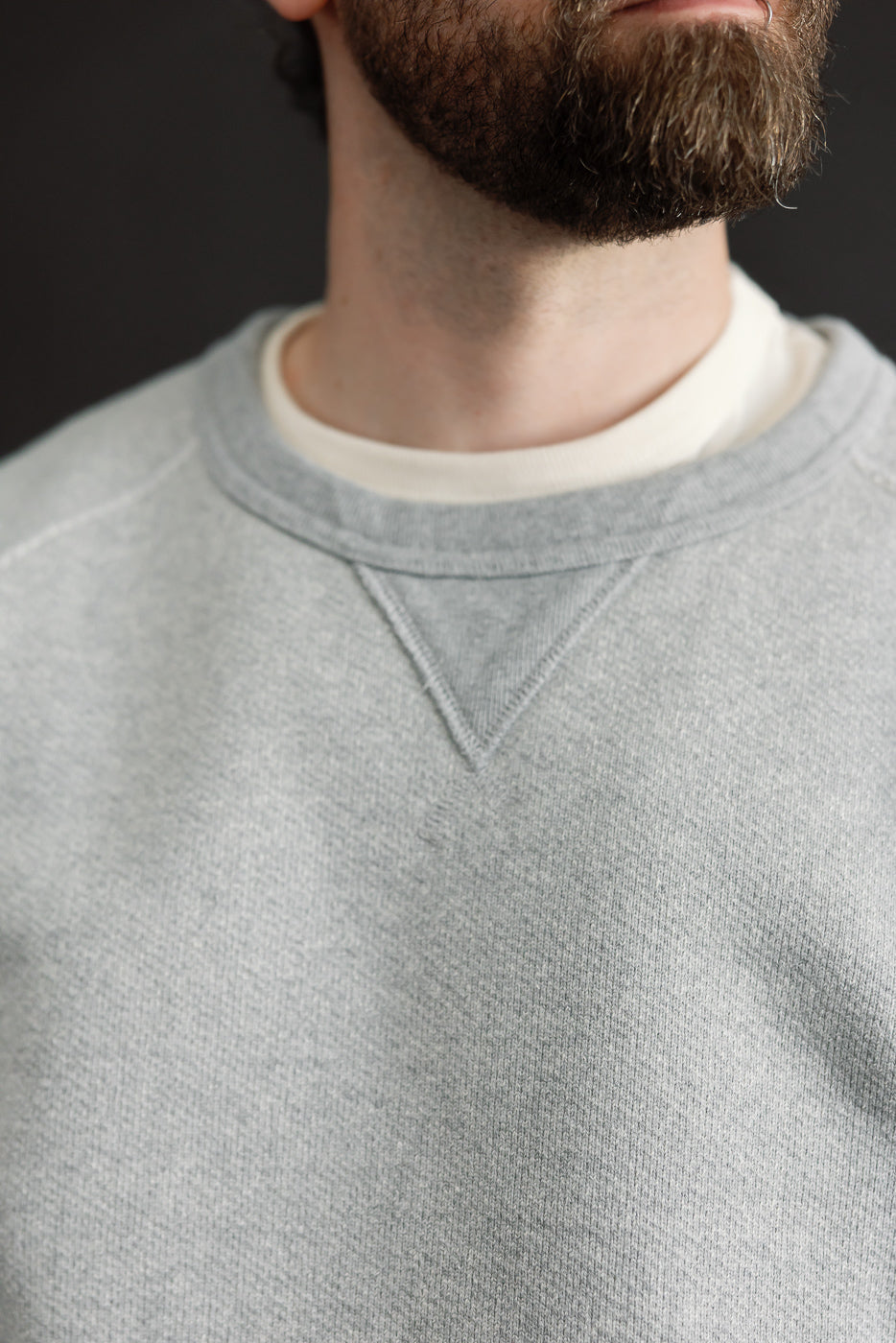 Close-up front view of a grey crewneck sweatshirt's ribbed collar and V-stitch detail.