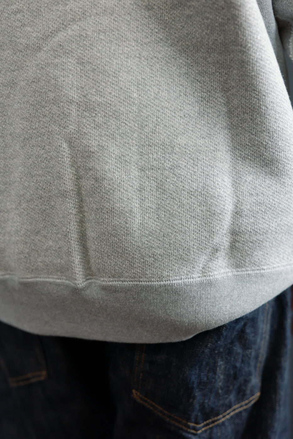 Close-up of the front hem and fabric texture of a grey heathered sweatshirt.