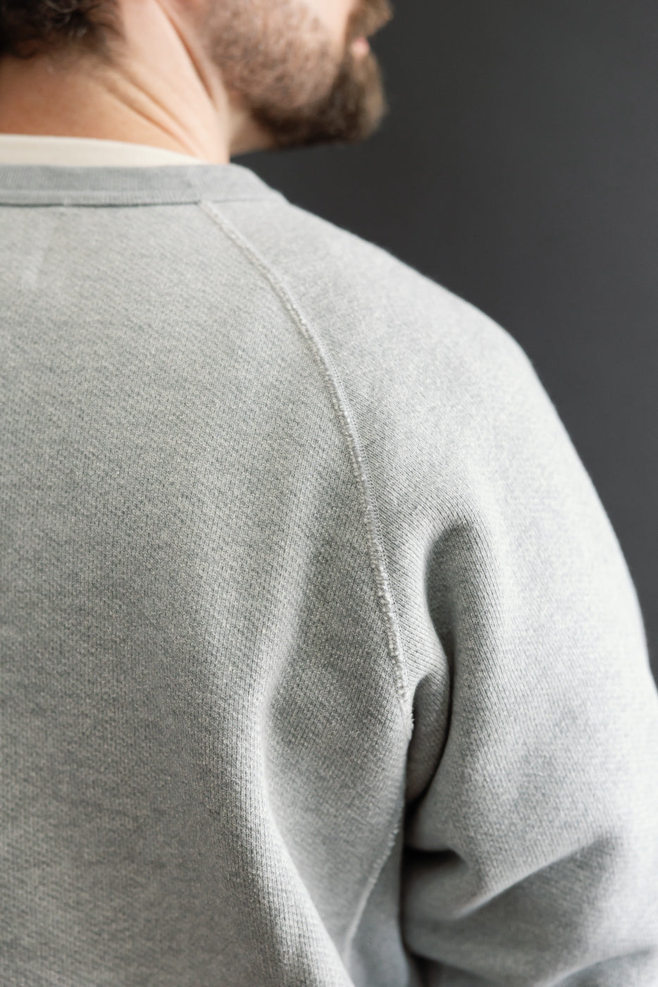 Close-up of the back of a male model's grey sweatshirt, showing fabric texture and shoulder seam.