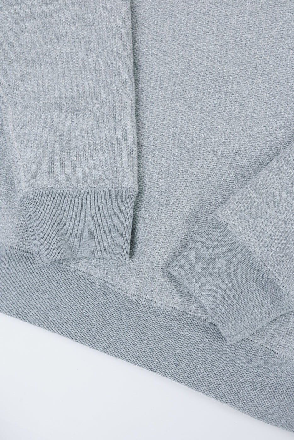 Close-up of the ribbed cuffs and textured grey fabric of a sweatshirt's sleeves.