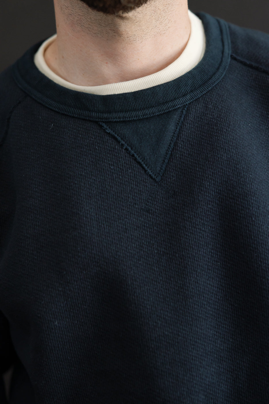 Close-up front view of a male model's neckline wearing a navy blue crewneck sweatshirt with ribbed collar.
