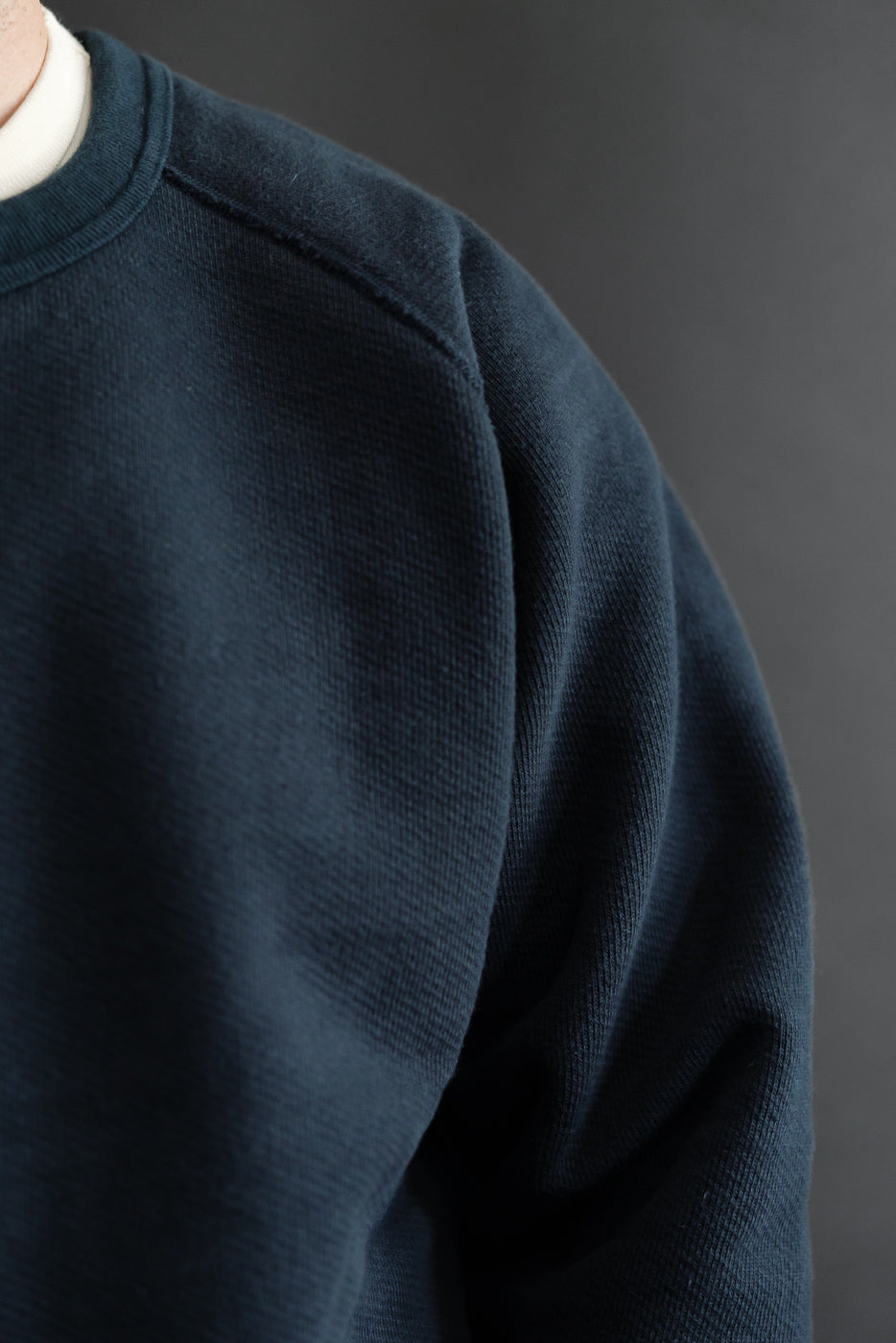 Close-up of the left shoulder and sleeve texture on a navy blue crewneck sweatshirt.