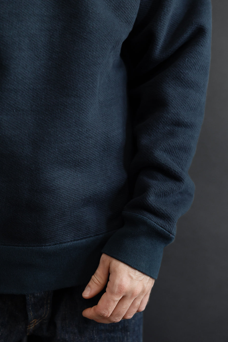 Close-up side view of a navy blue ribbed fabric sweatshirt sleeve and hem on a male model.