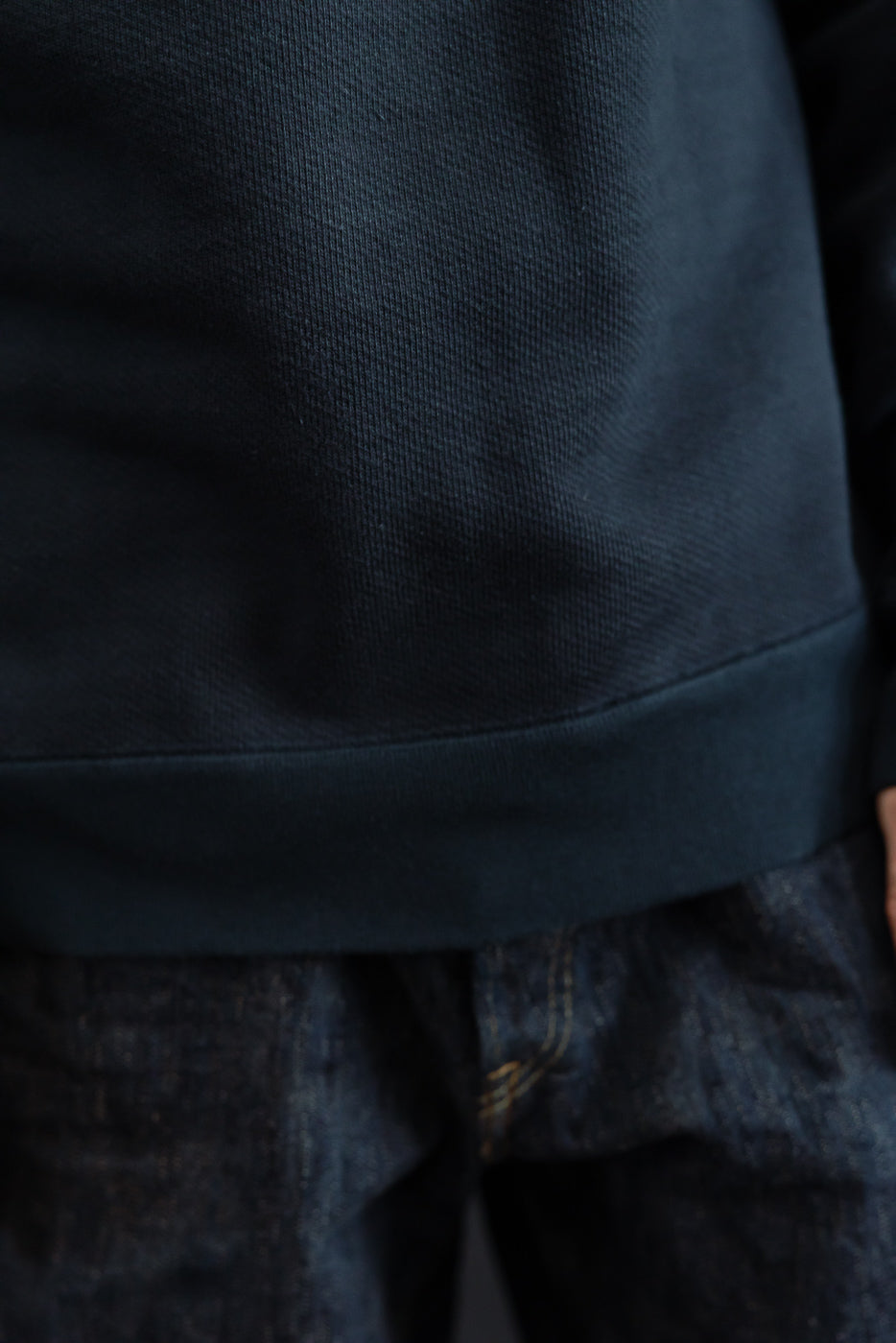 Close-up of the front hem and fabric texture of a navy blue sweatshirt and selvedge denim jeans.