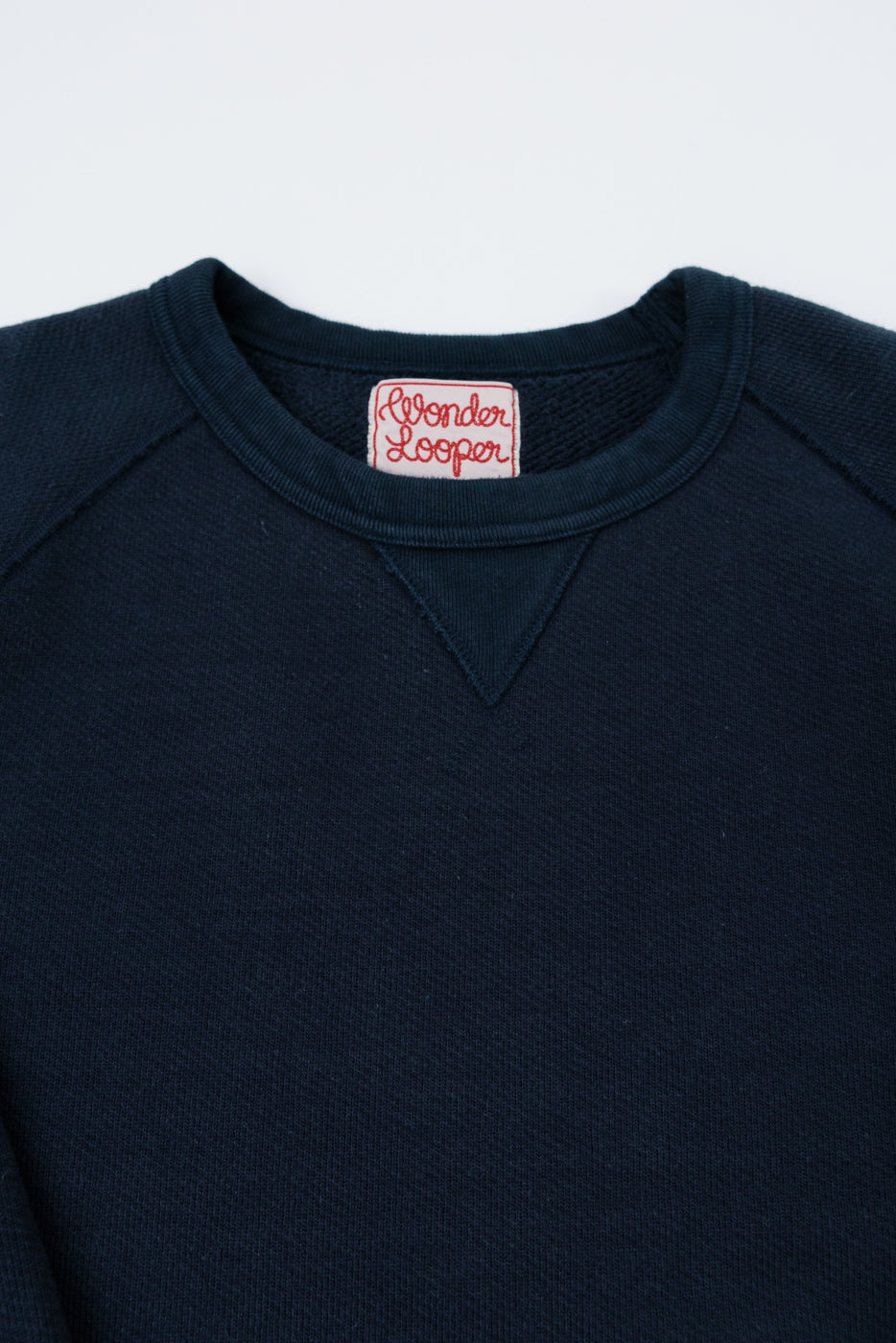 Close-up front view of a navy blue crewneck sweatshirt showing the ribbed collar and brand tag.