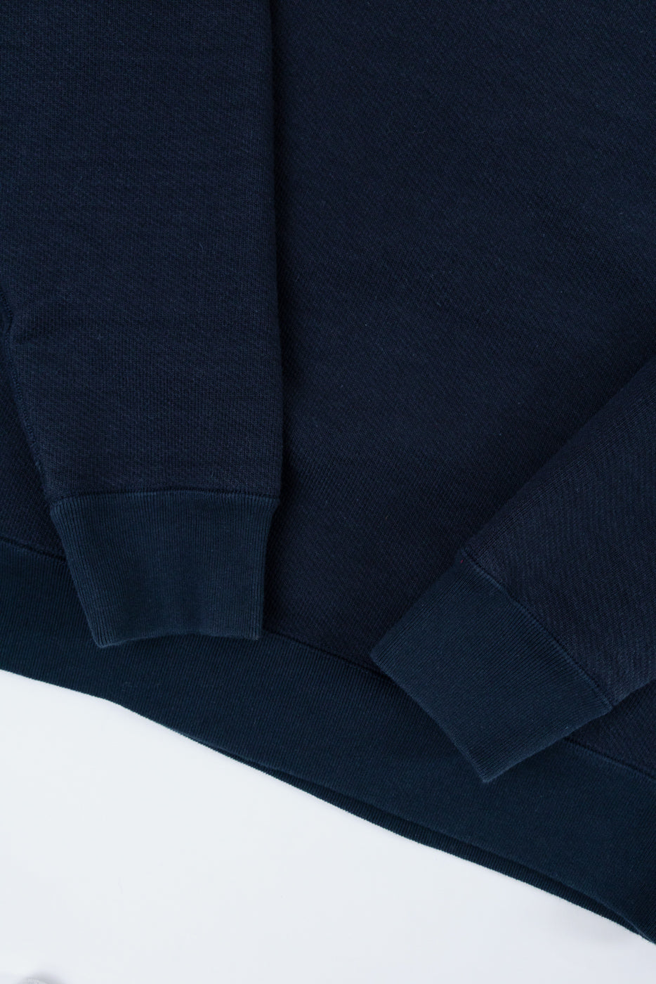 Close-up of a navy blue sweatshirt's ribbed cuffs and bottom hem on the front side.
